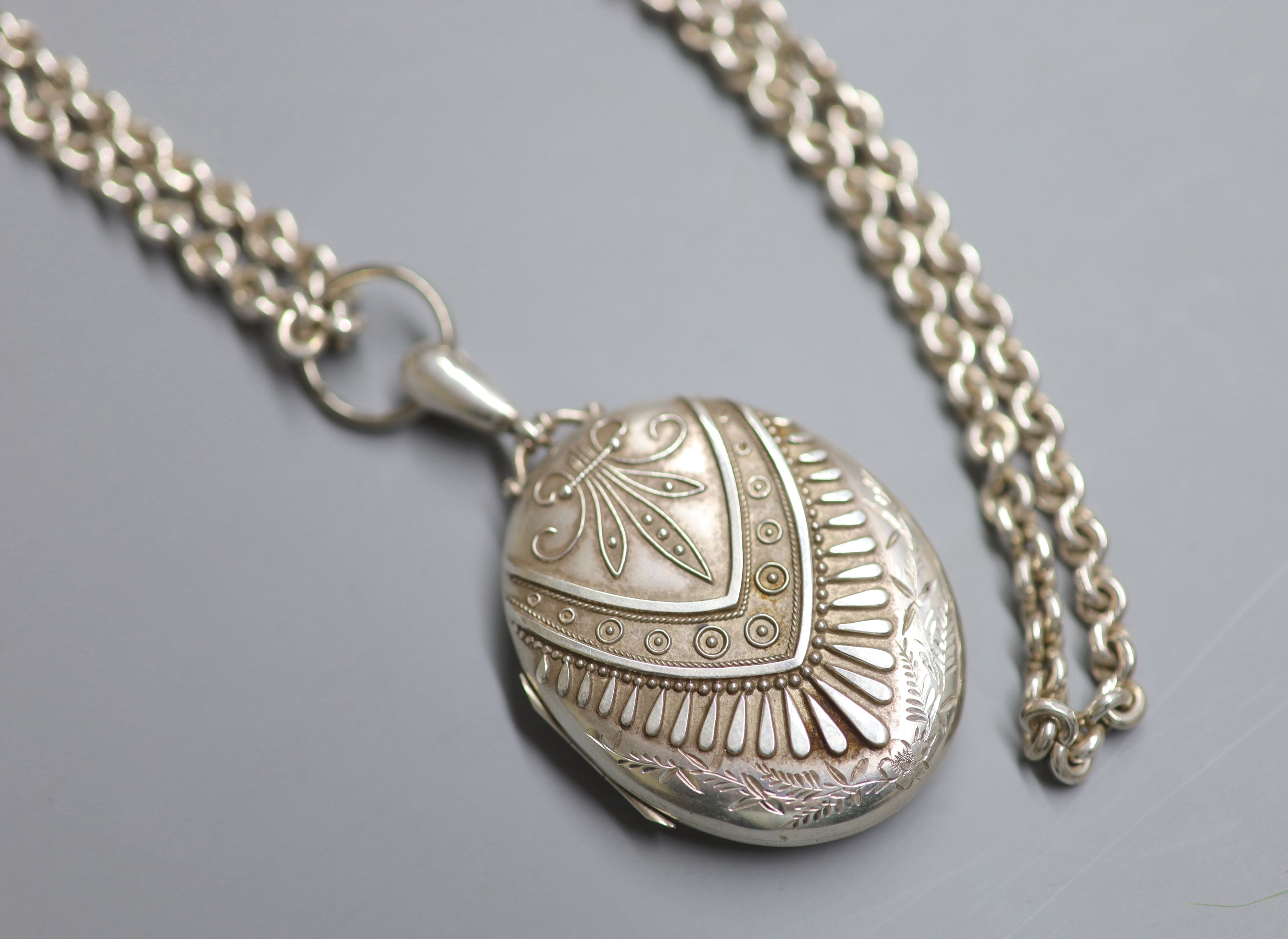 A late Victorian silver oval locket, 47mm, on a long white metal chain, 148cm, gross 124 grams.